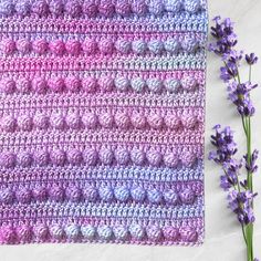 a crocheted square with purple flowers next to it