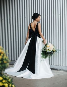 a woman in a black and white wedding dress holding a bouquet with her back to the camera