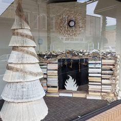 a window display with books and a fake christmas tree in the front, behind which is a fireplace