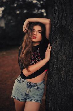 a young woman leaning against a tree with her arms on the back of her head