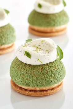 three green desserts with whipped cream and leaves on top are arranged on a white surface