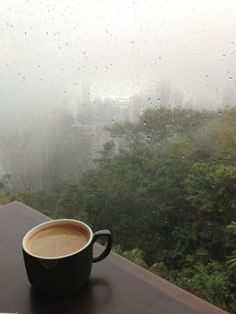 a cup of coffee sitting on top of a table next to a window covered in rain