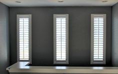 an empty room with three windows and white shutters