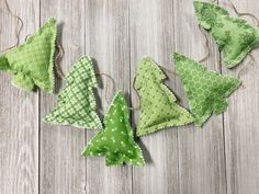 four green fabric christmas trees hanging from twine on wooden floor next to string and pegs