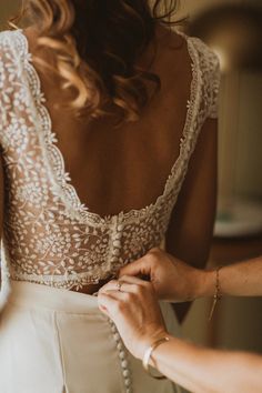 a woman in a wedding dress is helping another woman put something on her bral