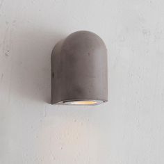 an outdoor wall light mounted on the side of a white stucco wall with a grey shade