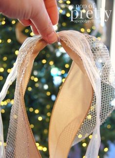 a hand is holding a pair of ballet shoes in front of a christmas tree