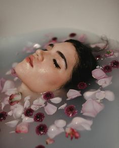 a woman laying in a bath filled with water and lots of pink flowers on the floor