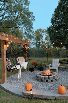 an outdoor fire pit surrounded by chairs and lights with pumpkins on the ground next to it