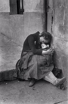 black and white photograph of a woman holding a child on her lap, leaning against a wall