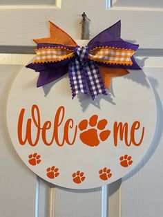 a welcome sign with an orange and purple bow hanging from the front door, decorated with paw prints