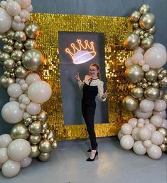 a woman standing in front of a gold and white photo frame with balloons around it