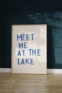 a poster with the words meet me at the lake in blue ink on a wood floor