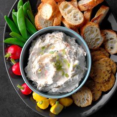 a bowl of dip surrounded by crackers and vegetables