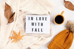 the words in love with fall written on a sign next to autumn leaves and a cup of coffee