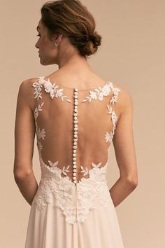 the back of a woman's wedding dress with flowers on it and pearls hanging down