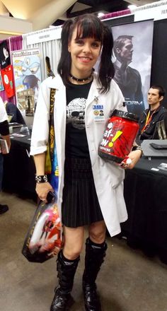 a woman in black and white outfit holding a bag next to a table with posters on it