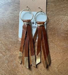 two pairs of leather tasseled earrings on a wooden table with a tag attached to it