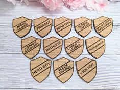 six wooden badges with the words head boy and ten other ones on them, sitting next to pink flowers