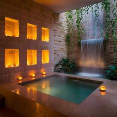 an indoor hot tub with candles lit in front of it and water running down the wall