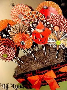 an arrangement of paper fans and pumpkins in a basket with ribbon on the top