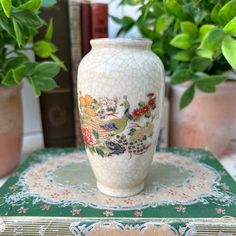 a white vase sitting on top of a table next to potted plants and books