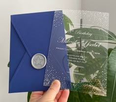 a person holding up a blue and white wedding card with a silver star on it