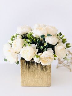 white flowers are sitting in a gold vase