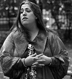 black and white photograph of a woman standing in the street with her hands folded out