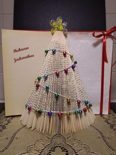 an origami christmas tree made out of book pages and colored beads is displayed next to a greeting card