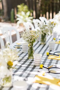 the table is set with white and black checkered cloths, yellow ribbon, vases filled with baby's breath flowers