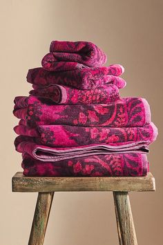 a stack of pink towels sitting on top of a wooden stool next to a wall