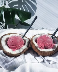 two coconuts with pink ice cream in them sitting on a towel next to a plant