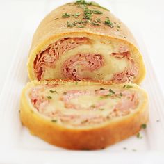 a ham and cheese roll on a white plate with parsley sprinkled around the edges