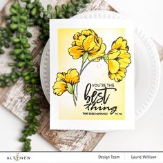 a white plate with yellow flowers on it next to some green leaves and a card