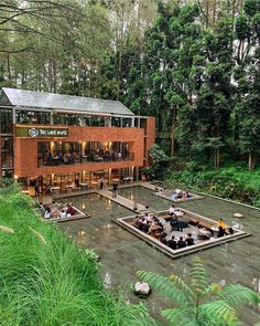 people sitting at tables in front of a building surrounded by trees and greenery on a rainy day