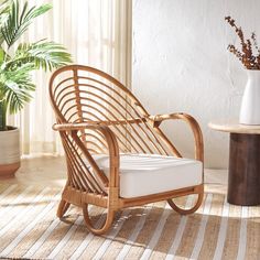 a wicker rocking chair with white cushions in front of a potted palm tree