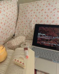 a laptop computer sitting on top of a bed next to an open book and candle