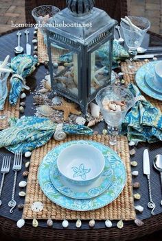 the table is set with blue and white dishes, silverware, and seashells