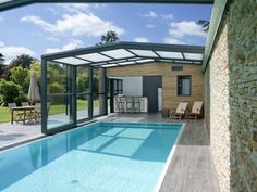 an empty swimming pool in front of a house with glass walls and doors on the side