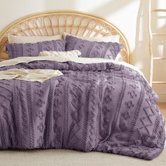 a bed with purple comforter and pillows in a room next to a wicker headboard