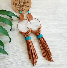 two tasseled earrings on a white table with a wooden sign that says, i am engaged with love