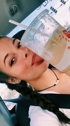 a woman drinking water out of a plastic cup in the back seat of a car