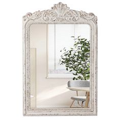 an ornate white framed mirror sitting on top of a table next to a potted plant