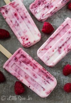 raspberry ice cream popsicles on a baking sheet with fresh raspberries