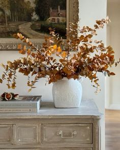 a white vase filled with leaves on top of a dresser