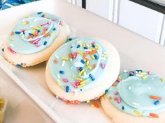 three frosted donuts with sprinkles in a white tray on a counter