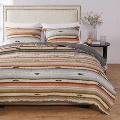 a bed with striped comforter and pillows on top of wooden floor next to window