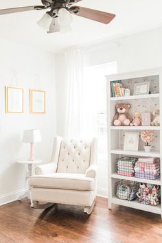 a white chair sitting in front of a window next to a book shelf filled with stuffed animals