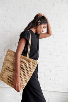 a woman carrying a wicker bag in front of a white brick wall with her hand on her head